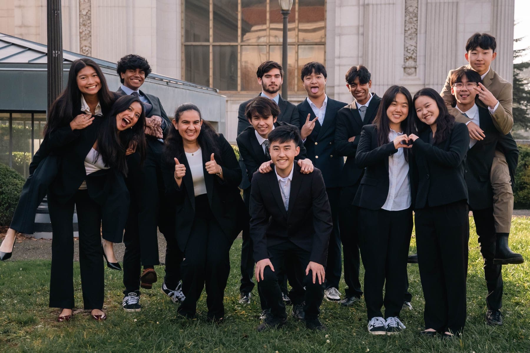The Acadev committee in business attire, posing and laughing together on the lawn outside a UC Berkeley campus building
