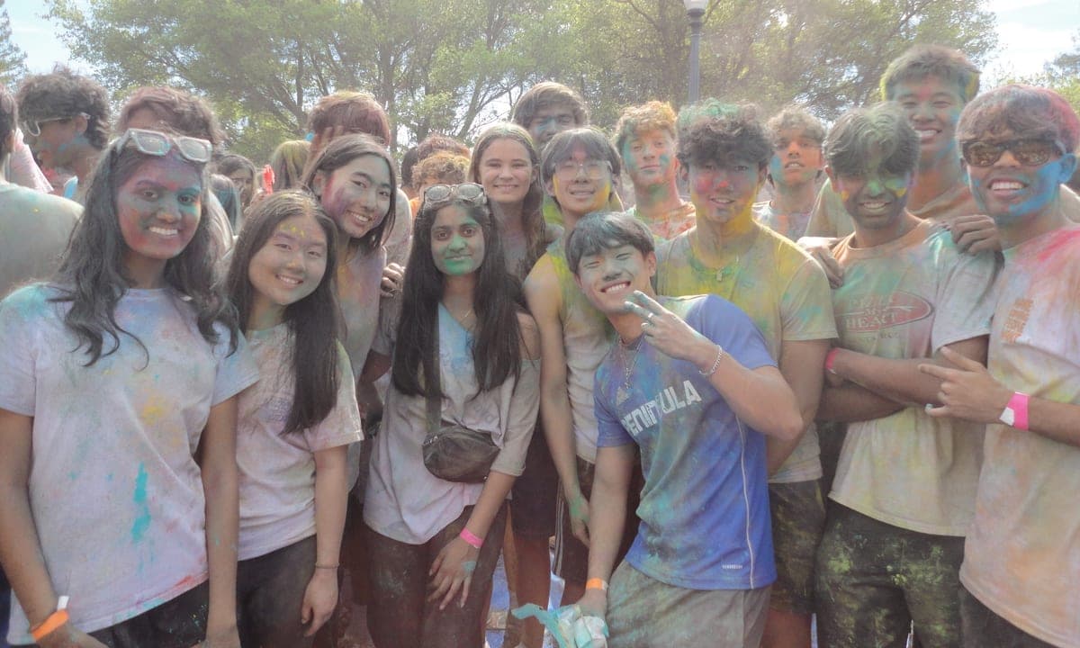 DSS members covered head to toe in coloured powder, crowded together and smiling at an outdoor Holi celebration